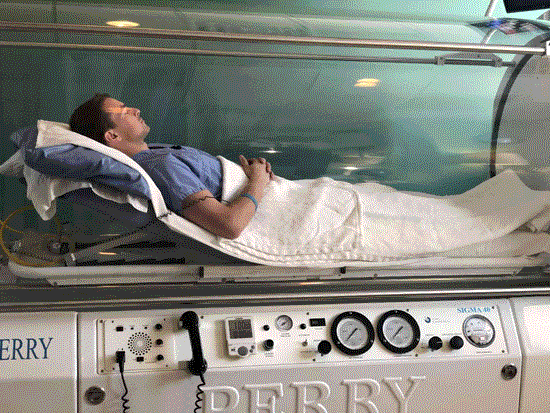 A man receiving Hyperbaric Oxygen Therapy while lying in a bed in a Dallas Metro Area clinic. 