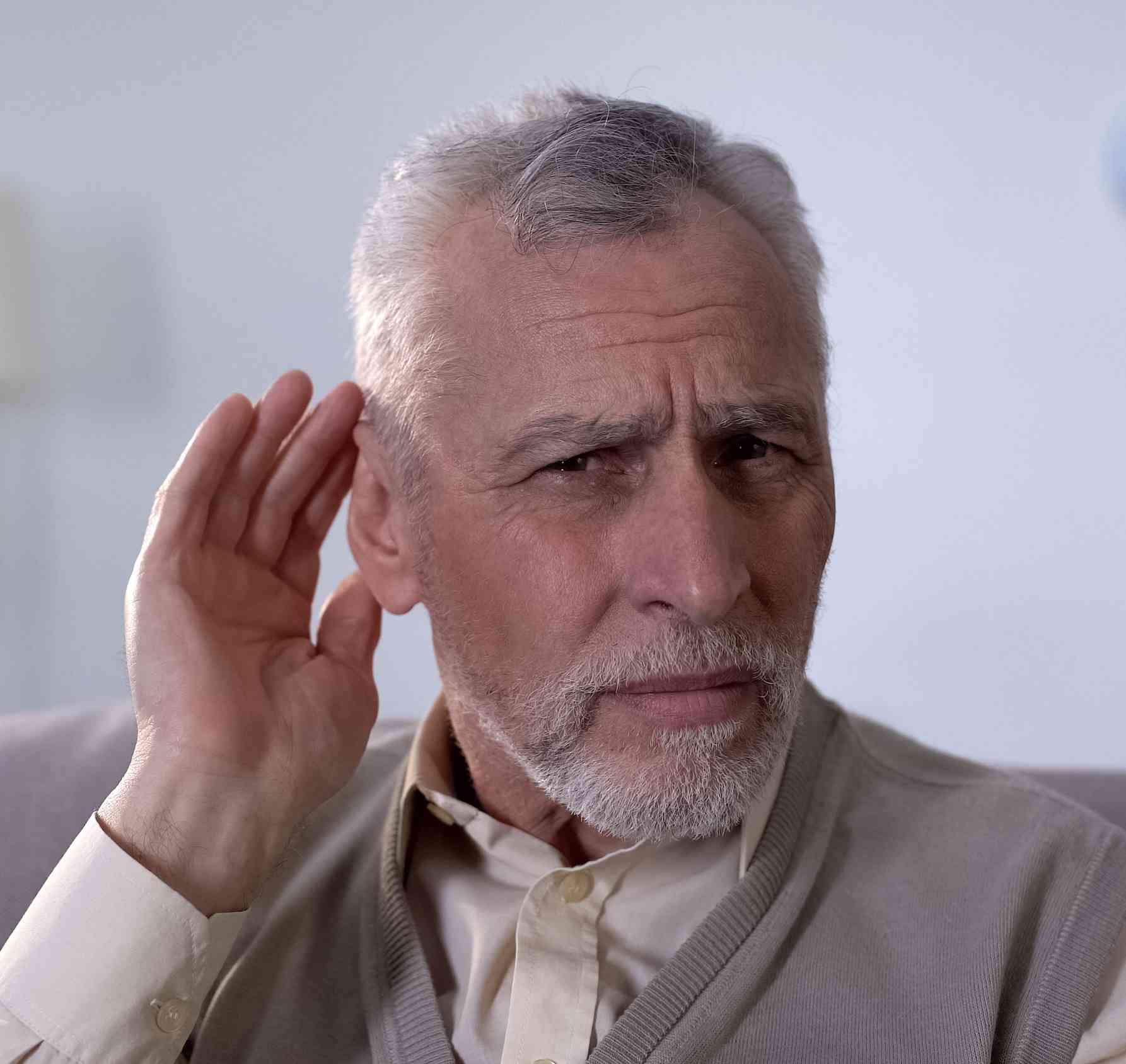 An older man with his hand to his ear due to sensorineural hearing loss in the Dallas Metro Area.
